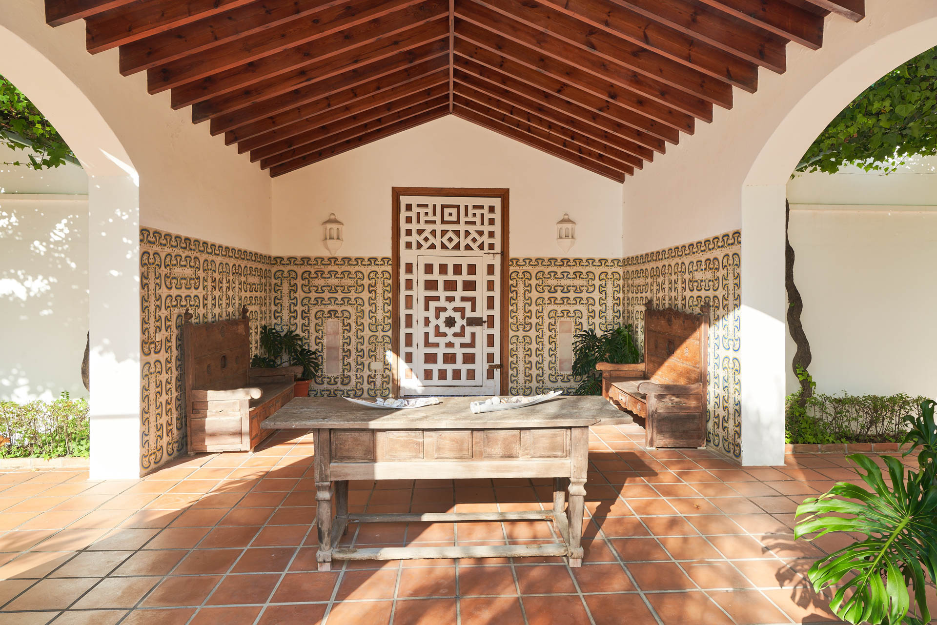 Imagen de un espacio con una puerta de madera, decorada con motivos geométricos y una mesa de madera.